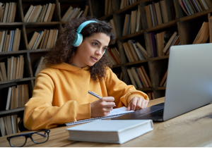 A teen girl wearing headphones uses a computer